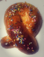 Cargar imagen en el visor de la galería, Mona de pascua en forma de lazo, decorada con anisetes de colores. La mona adquiere un bonito brillo gracias al glaseado que se le añade para pegar los anisetes. Es una masa abriochada y muy esponjosa, aromatizada con raspadura de naranja y limón, y zumo de naranja, productos que cultivamos en nuestra huerta.
